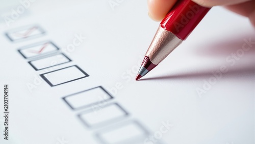 Hand marking checkbox on paper survey with red pen for assessment