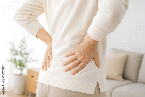 腰を押さえて腰痛に悩む人物の後ろ姿 自宅での健康イメージ