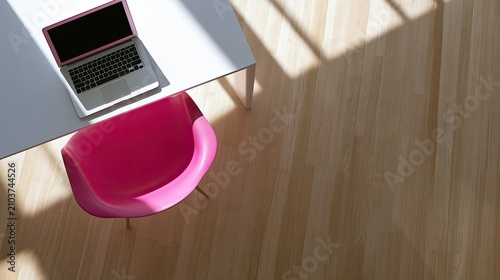 Bright pink chair and open laptop on a white desk with wood floor and sunbeams
