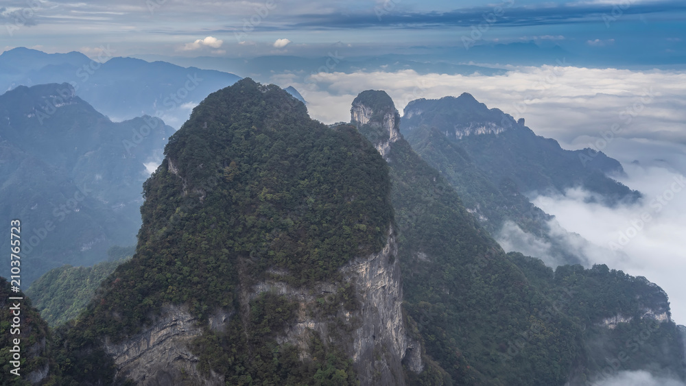 Obraz premium Picturesque mountain landscape. High cliffs. Green vegetation on steep slopes and peaks. Blue sky, clouds. China. Zhangjiajie. Tianmen Mountain