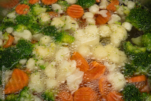 Vegetables boiling in water with bubbles and steam in a cooking pot on a stove