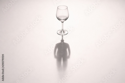 Transparent wine glass casting a shadow resembling a human figure on a textured surface, showcasing interplay of light and shadow in a minimalist composition