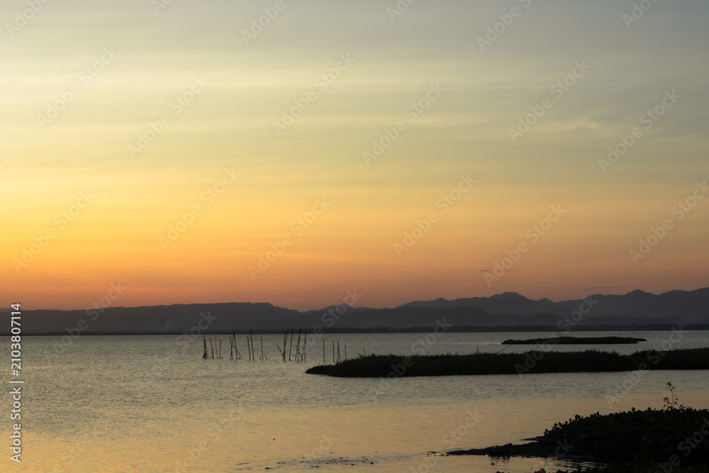 Obraz premium Sunset Over Calm Lake with Distant Mountains