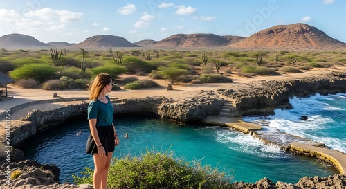 A woman stands on a cliff overlooking a serene turquoise lagoon