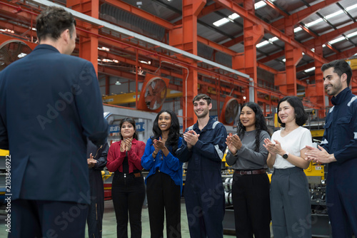 Group of male and female workers and manager standing discussing, meeting together in factory. Diverse corporate colleagues and multicultural in factory