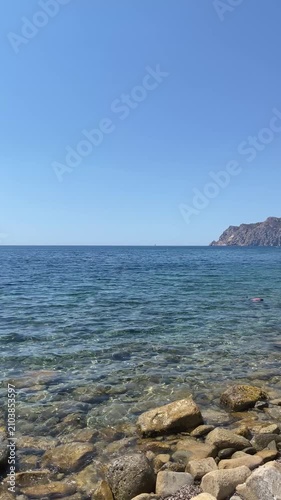 panoramic view of the rocky Cala de la Llobella in Benissa with crystal clear Mediterranean waters and the Penyal d'Ifach in the distance under a bright blue sky on a sunny summer day