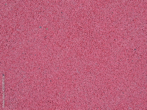 A seamless rubber surface of a rich pink-red color. The surface consists of finely pressed crumbs and has a porous, rough texture. This type of rubber crumb is used on sports grounds.
