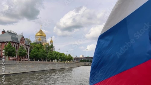 russian flag waving in foreground with cathedral of christ the saviour golden domes in background. moscow river flows past historic buildings and orthodox cathedral