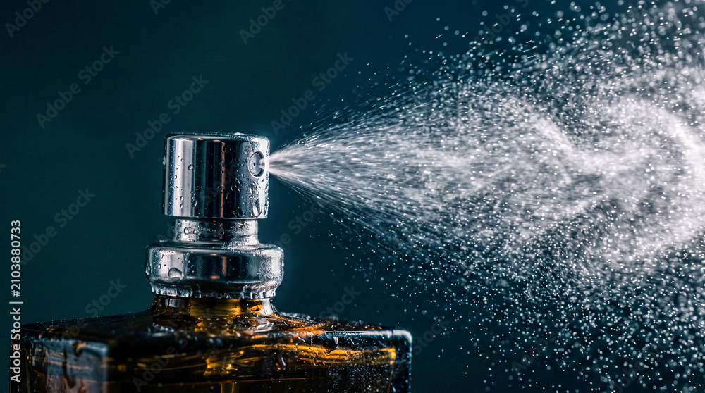 Obraz premium Close up of a perfume bottle spraying a fine mist against a dark background.