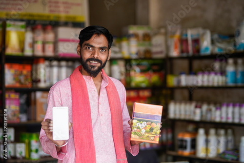 Photography Indian farmer showing fertilizer or seeds packets at shop