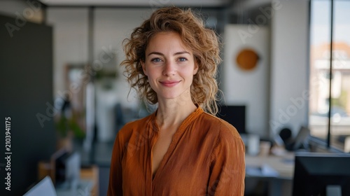 A young woman with curly blonde hair stands in an office setting,
