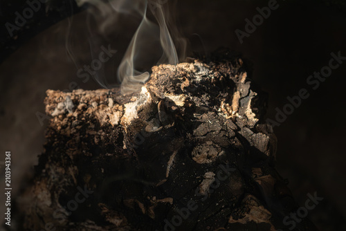 Close up shot of smoldering charcoal embers with thin white smoke rising against a dark background
