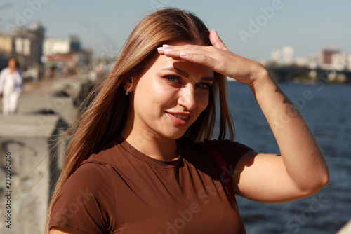 Close up portrait of a beautiful young woman with long light brown hair in a brown blouse against a blurred city river background in Kyiv