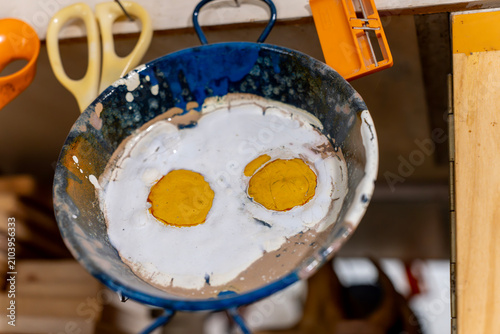 Foto Metal bowl coated with hot vitreous enamel layers imitating a fried egg design with two yolks, hanging on a workshop wall