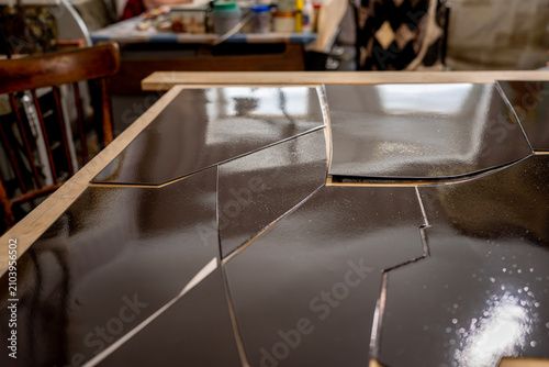Quadro su tela Glossy metal plates coated with dark vitreous enamel layer during production process on a wooden workbench inside a jewelry or artisan craft workshop