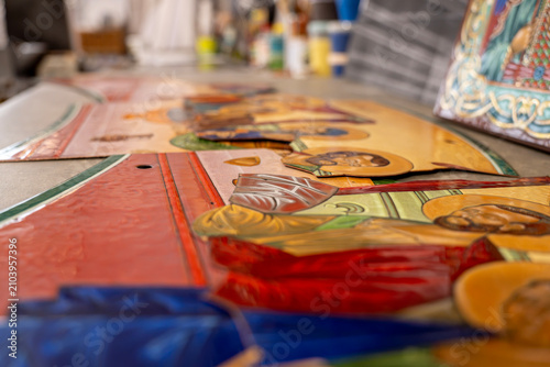 Фотография Metal plates with religious icons created using hot vitreous enamel technique on a workshop table, close up with selective focus on detailed enamelwork surfaces