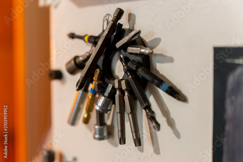 Collection of various interchangeable screwdriver bits, torx bits, and hex sockets attached to a round magnetic tool holder on a wall inside a workshop.
