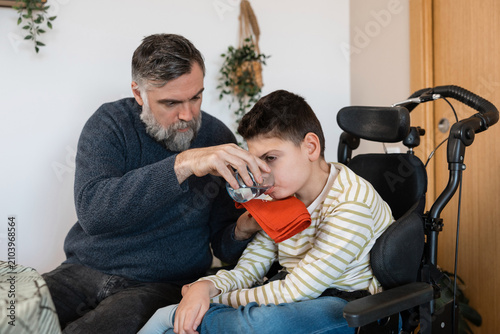 Father helping boy with cerebral palsy drink water