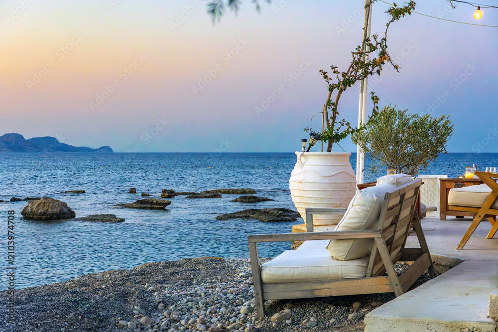 Obraz premium Cozy seaside lounge terrace with comfortable seating with traditional amphora pot overlooking the Mediterranean Sea at sunset in Kolymbia Rhodes