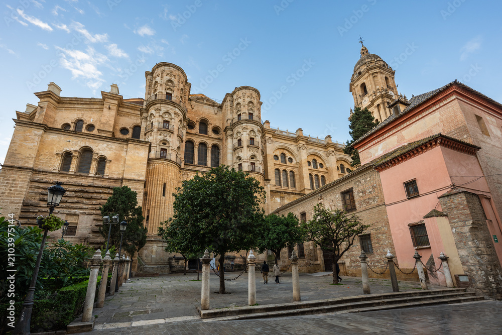 Fototapeta premium Low angle perspective of the majestic facade and bell tower of the Malaga Cathedral (Catedral de la Encarnación) under a partly cloudy sky, from a quiet square.