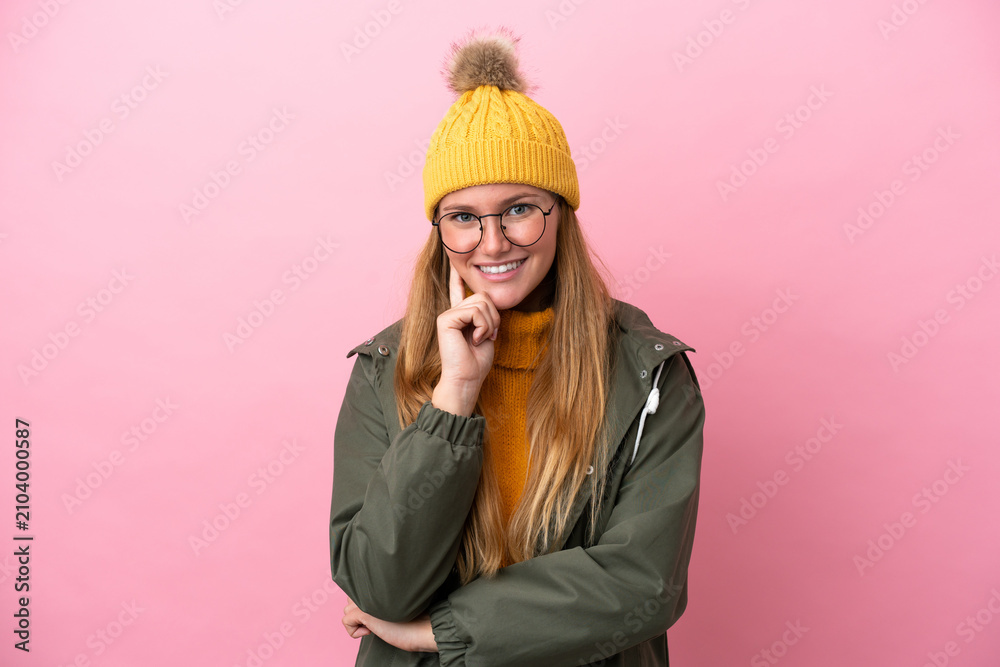 Obraz premium Young blonde woman wearing winter jacket isolated on pink background with glasses and smiling