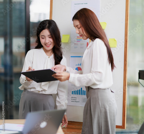 Professional businesswomen collaborating on a financial report, analyzing data and discussing sales strategy during a corporate meeting in a modern office environment