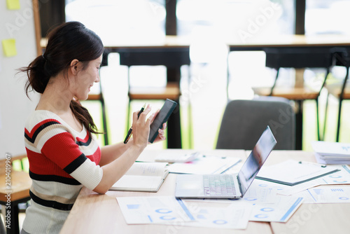 Asian businesswoman analyzing financial data. Performing calculations with a tablet and pen. Working on a laptop. And reviewing important documents