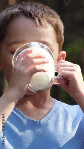 Child drinking milk outdoors. Young boy enjoys fresh milk in nature. Bright sunlight creates cheerful atmosphere. Vertical composition highlights joyful moment.