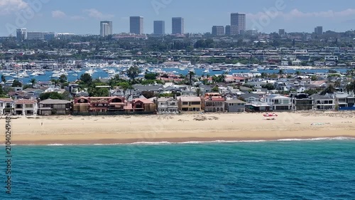 flying southbound along Balboa Beach located on Harbor Island, a small artificial island in Newport Beach, California, while massive waves hitting the wide sandy beach and people sunbathing