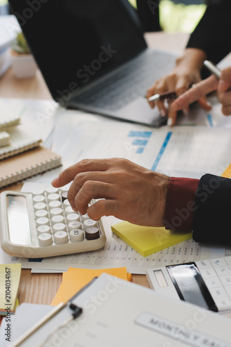 Accountant reviewing printed financial reports at messy office desk with calculator and sticky notes under soft window daylight for audit and corporate finance work