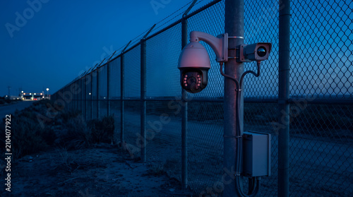 Security dome camera mounted on fence monitoring industrial perimeter at dusk
