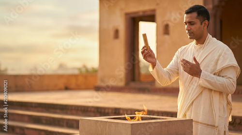 Indian priest performing fire ritual - Hindu man performing ritual prayer with fire offering at sunset  