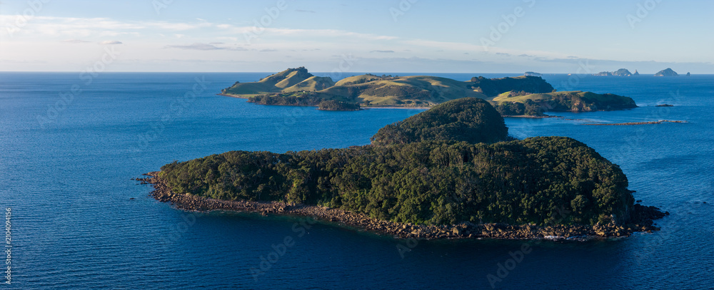 Obraz premium A panoramic view of the islands and coastline of Slipper Island, Coromandel Peninsula,, New Zealand, under a clear sky. The deep blue ocean surrounds the lush green islands