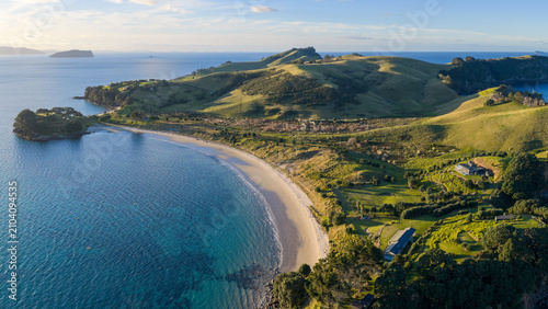 Aerial view of the stunning coastline and Slipper Island near Tairua, New Zealand. The clear blue ocean meets the green, rolling hills of the land.
