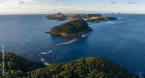 A panoramic view of the islands and coastline of Slipper Island, Coromandel Peninsula,, New Zealand, under a clear sky. The deep blue ocean surrounds the lush green islands