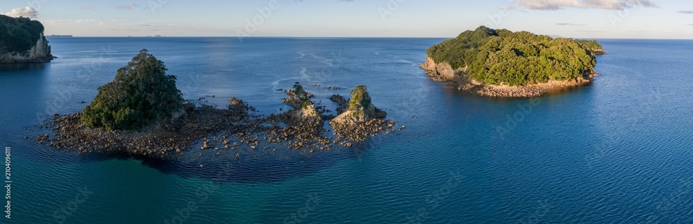 Fototapeta premium Scenic view of iDonut sland in the ocean near Whangamata, New Zealand.. The islands are covered in lush green trees and surrounded by deep blue water.