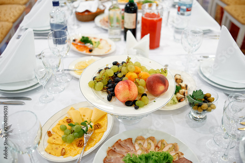 Billede på lærred An elegant banquet table arranged with fresh fruit, grapes, peaches, cheese and assorted appetizers, set with glassware and napkins for a formal dinner, celebration or catered event