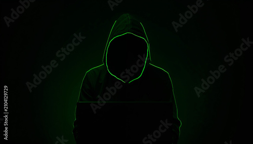 黒いフードを纏い鮮やかな緑のネオン光に縁取られた顔のないハッカーが暗い画面の前に座る