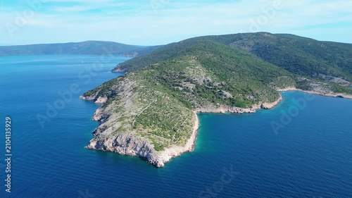 Aerial view of a stunning Adriatic island coastline with lush green hills, rocky shores, and crystal-clear turquoise waters under a summer sky.