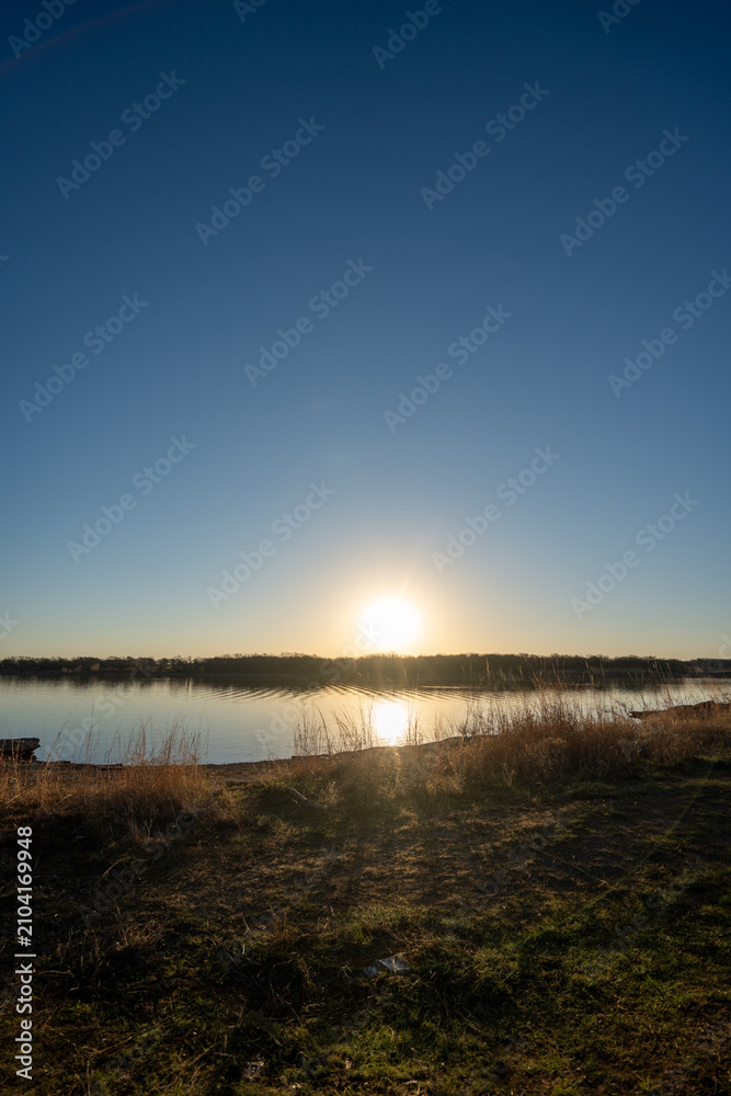 Fototapeta premium Golden sun glows over calm lake surface