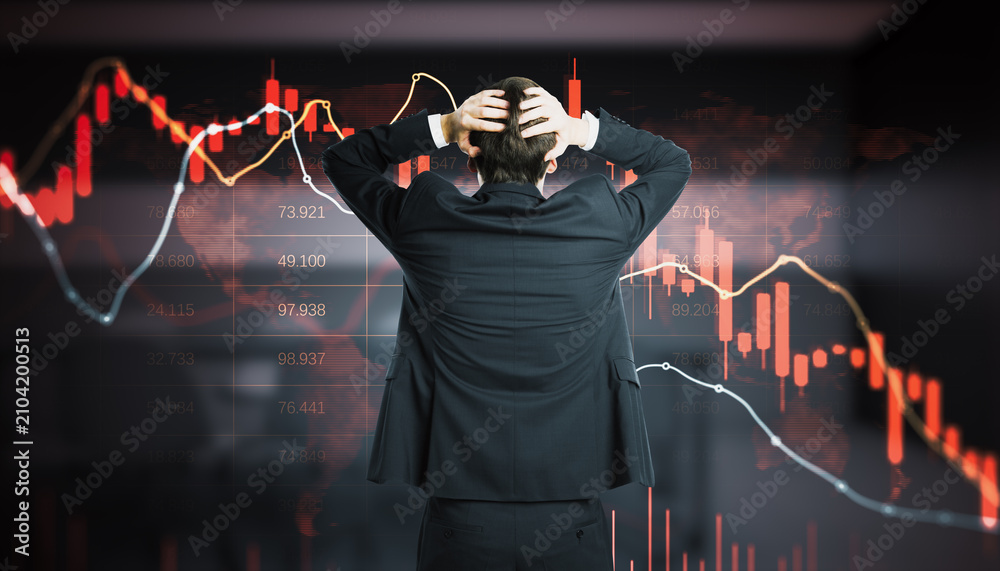Obraz premium Stressed businessman holding head in hands facing screen with red falling candlestick charts and numbers, stock market crash and trader panic concept.