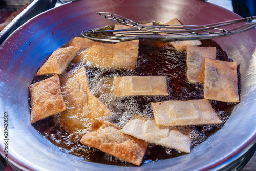 Close up of golden brown pastel fried dough being lifted from hot oil in a large pan at a street food market