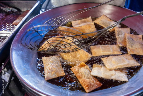 Close up of golden brown pastel fried dough being lifted from hot oil in a large pan at a street food market