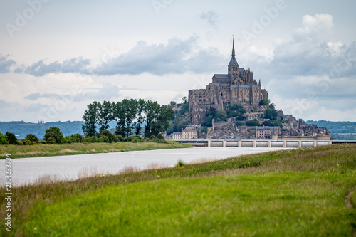 Photography Mont-Saint-Michel viewed from canal with bridge crossing, green fields and trees, landscape, UNESCO heritage site