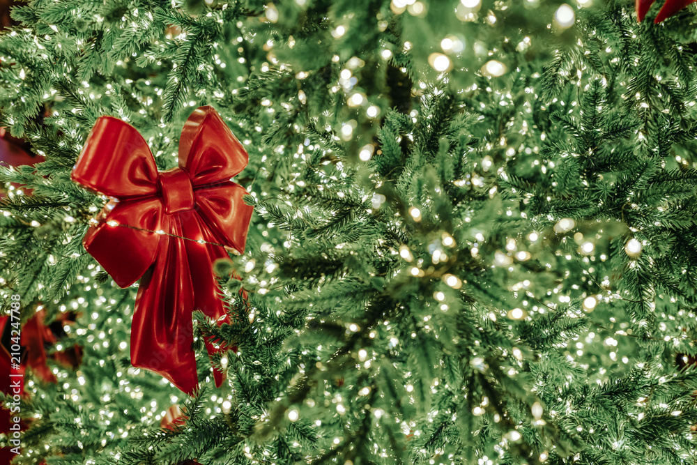 Obraz premium Red bright Christmas bow hanging on a decorated Christmas tree, festive holiday seasonal golden green background