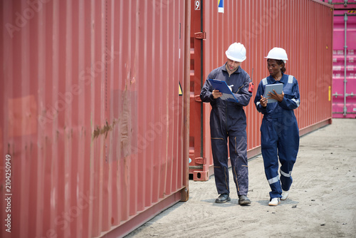 Workers holding a clipboard and inspecting a large shipping container.