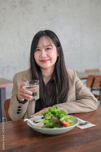 Smiling Asian Woman Holding a Glass of Water Next to a Fresh Salad