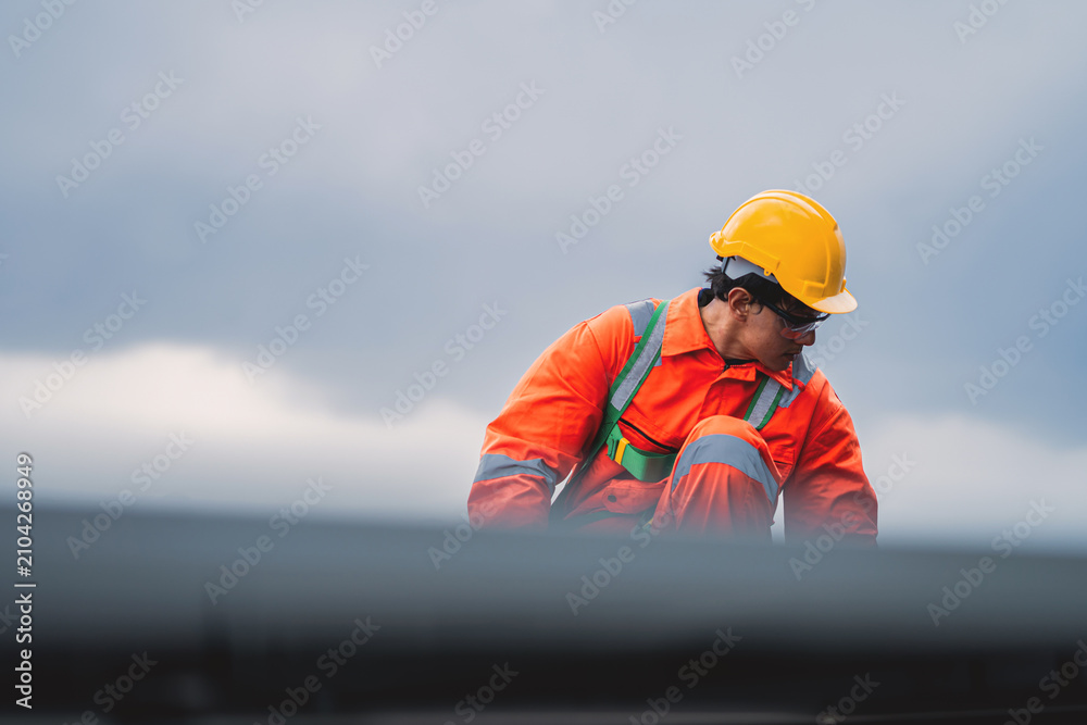 Obraz premium Asian Male Engineer in Orange Safety Suit Cleaning Solar Panel Surface on Rooftop. Solar Panel Maintenance and Cleaning in Renewable Energy Operations.