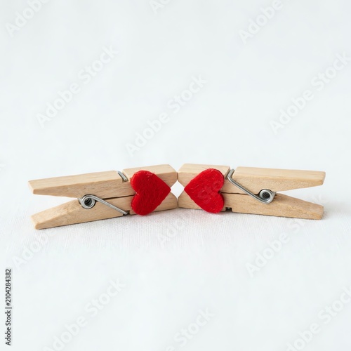 Two wooden clothespins holding small red hearts against white background, love concept