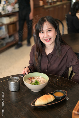 High-Angle Shot of a Smiling Asian Woman with Noodle Soup and Bread Roll